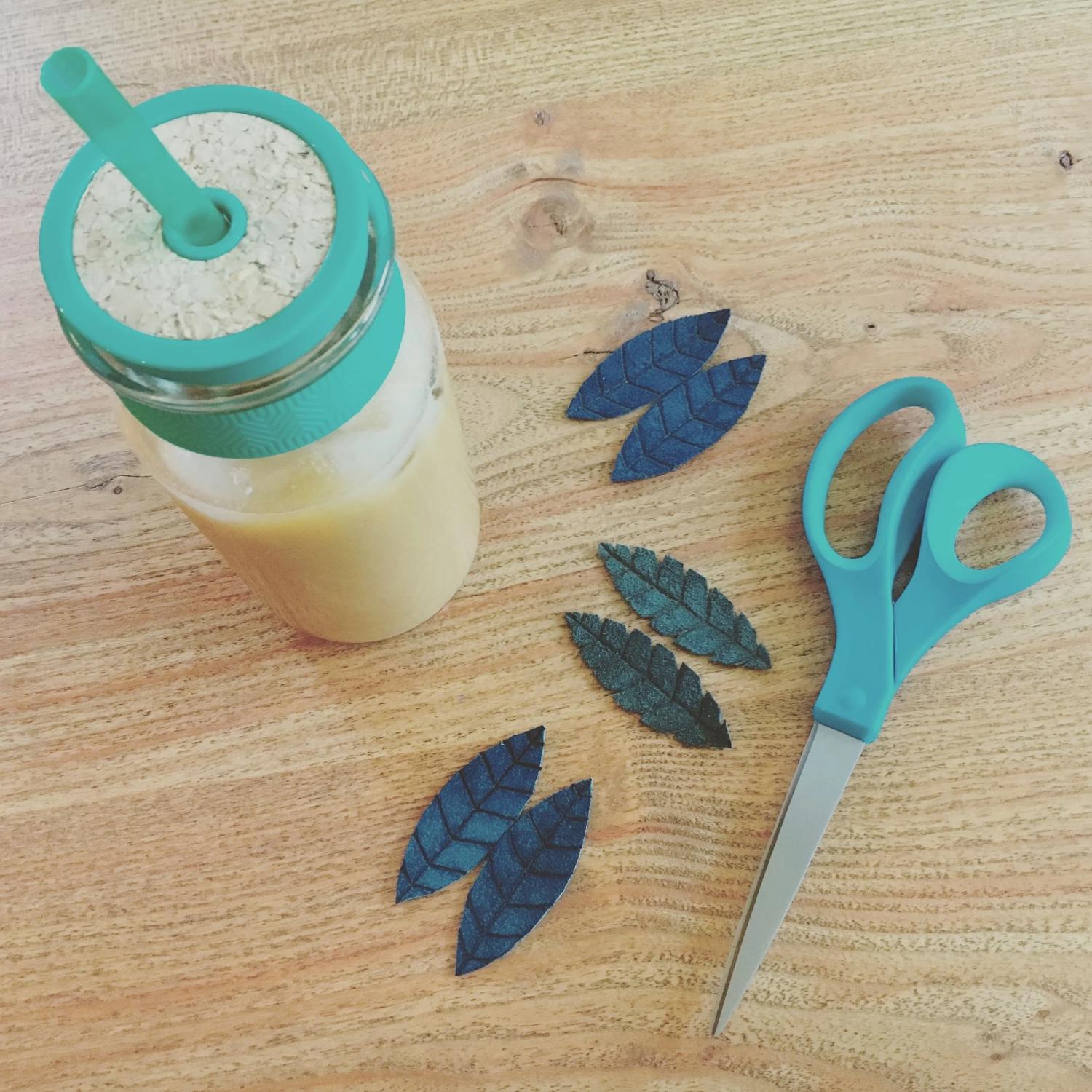 Teal scissors and blue leather leaves on a wood table